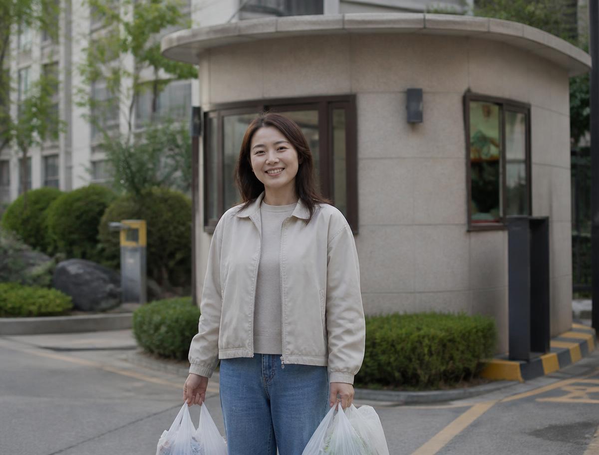 아파트 경비실 앞에서 쇼핑백 두 개를 든 주민이 웃고 있는 모습